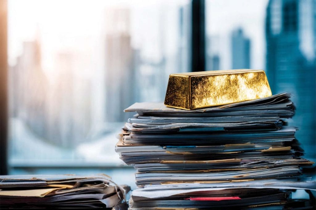 Rachat or : vendre bijoux, pièces et lingots au bon prix 2 Un lingot d'or posé sur une pile de journaux devant des immeubles de bureaux